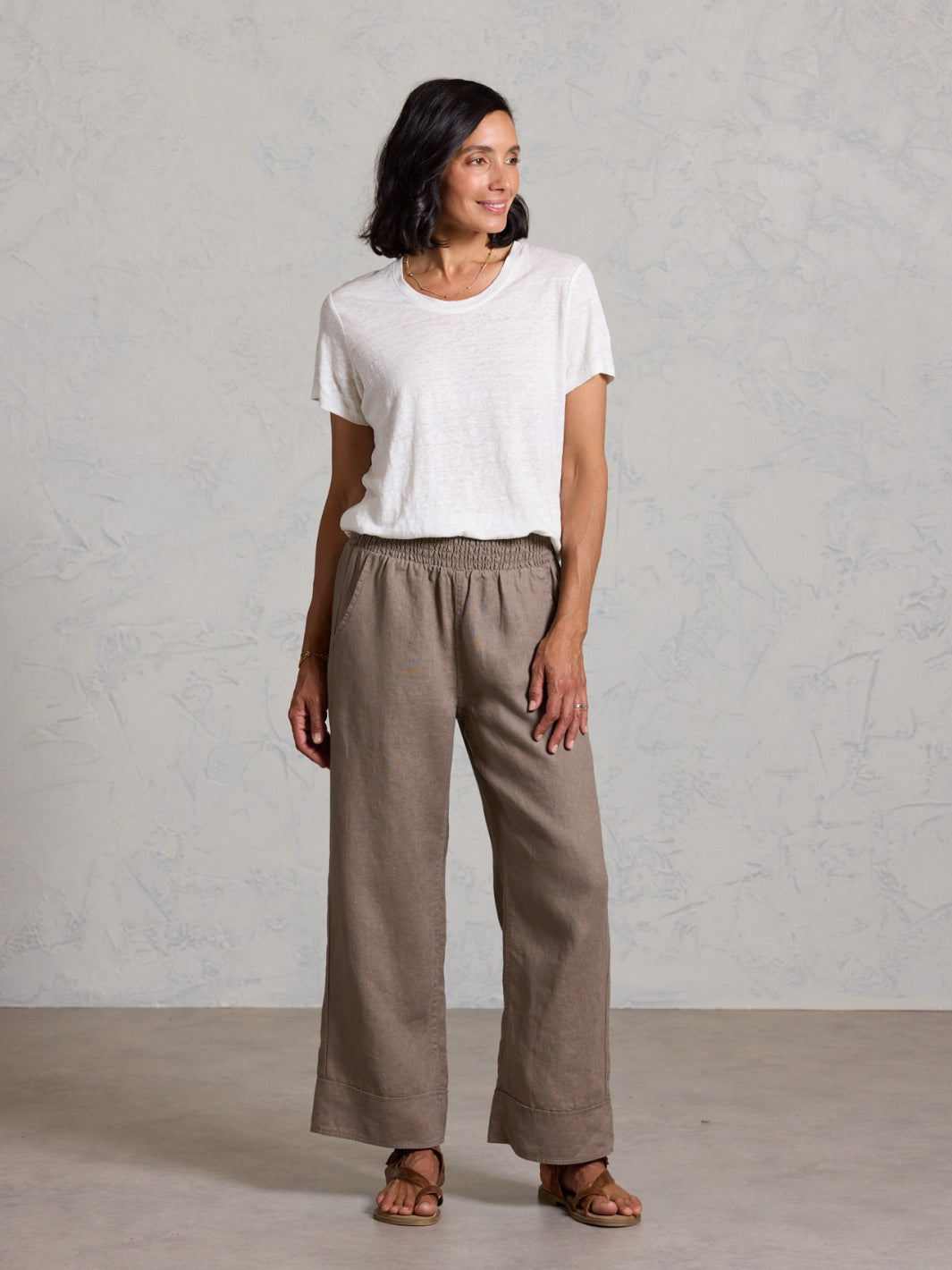 Woman wearing a white t-shirt and brown pants against a plain background