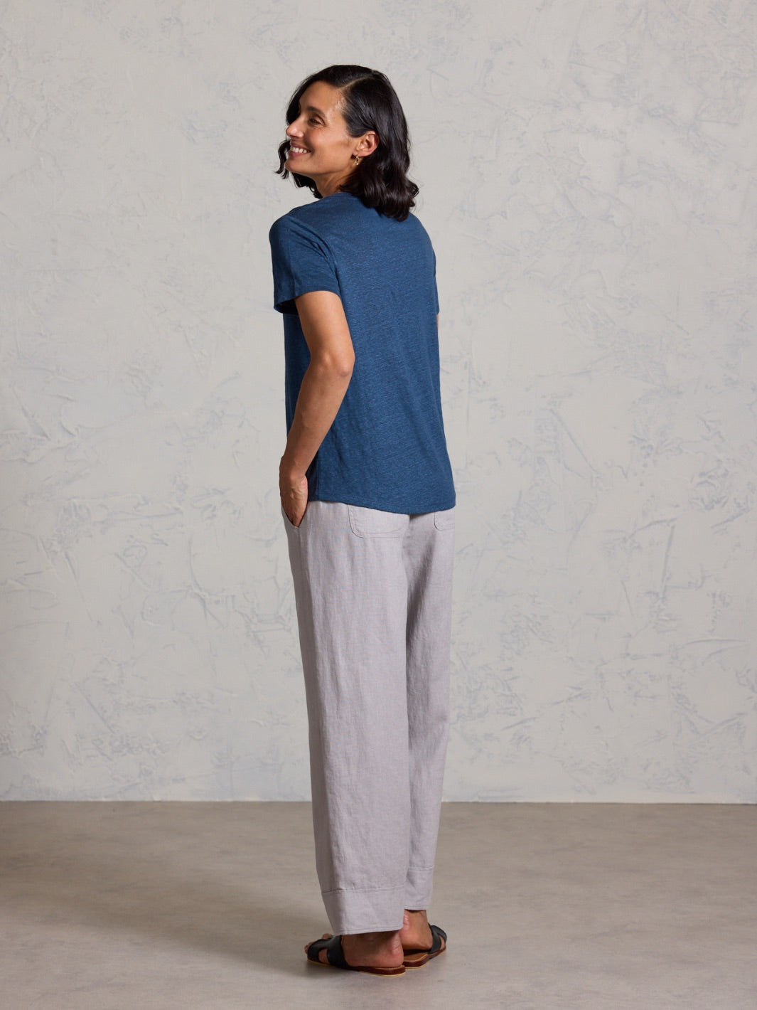 Woman wearing a blue shirt and light gray pants against a plain background