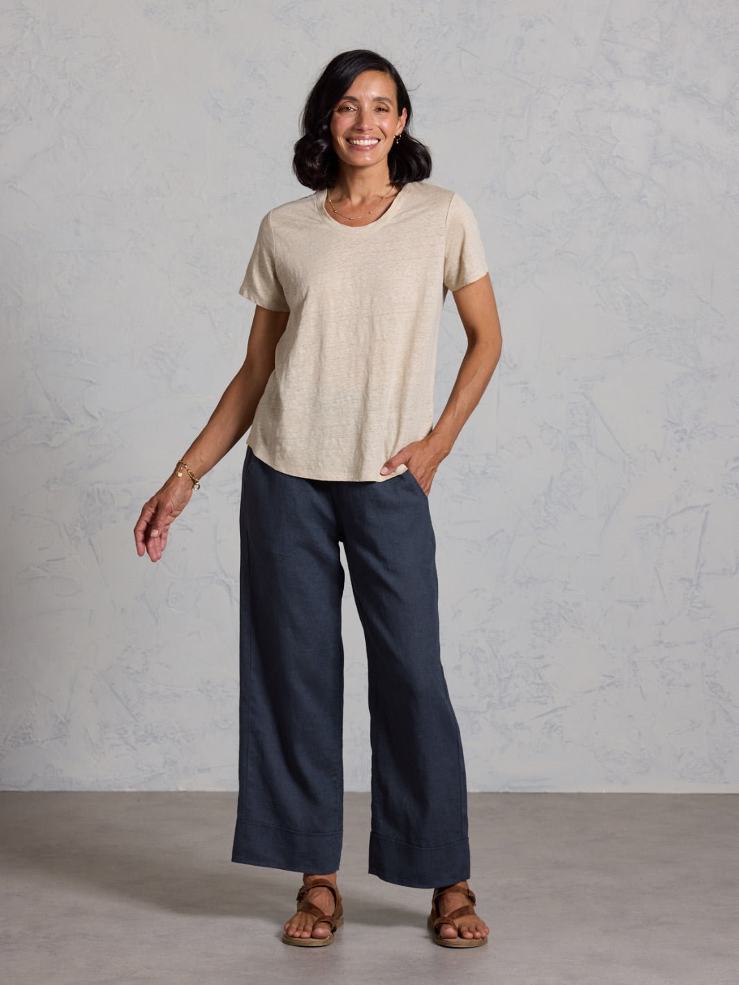 Woman wearing a beige top and black pants against a gray background