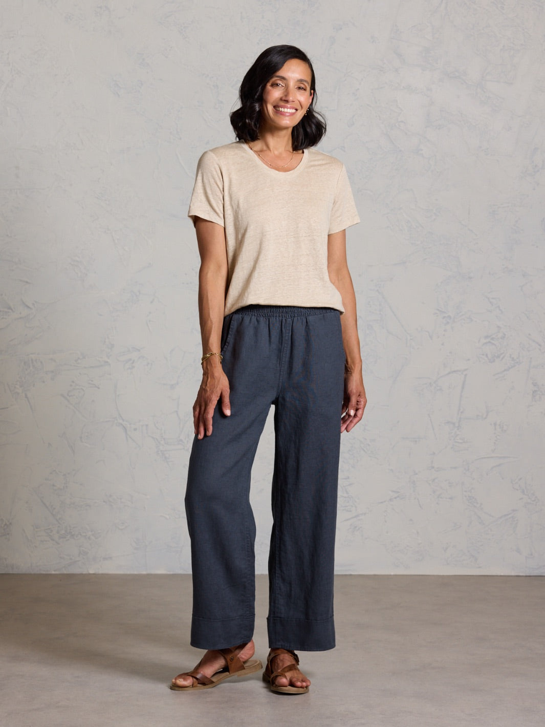 Woman wearing a beige top and black pants against a gray background