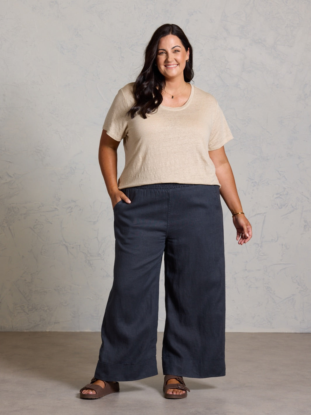 Woman wearing a beige top and black pants against a plain background