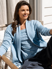 Woman wearing a light blue cardigan sitting outdoors.