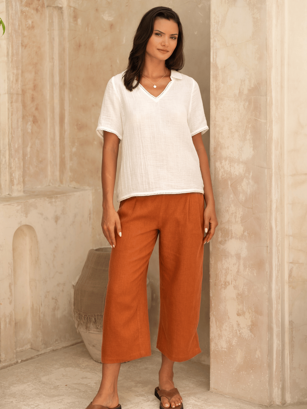 A woman modeling a white Henley cotton top with short sleeves and a V-neckline, paired with brown trousers.