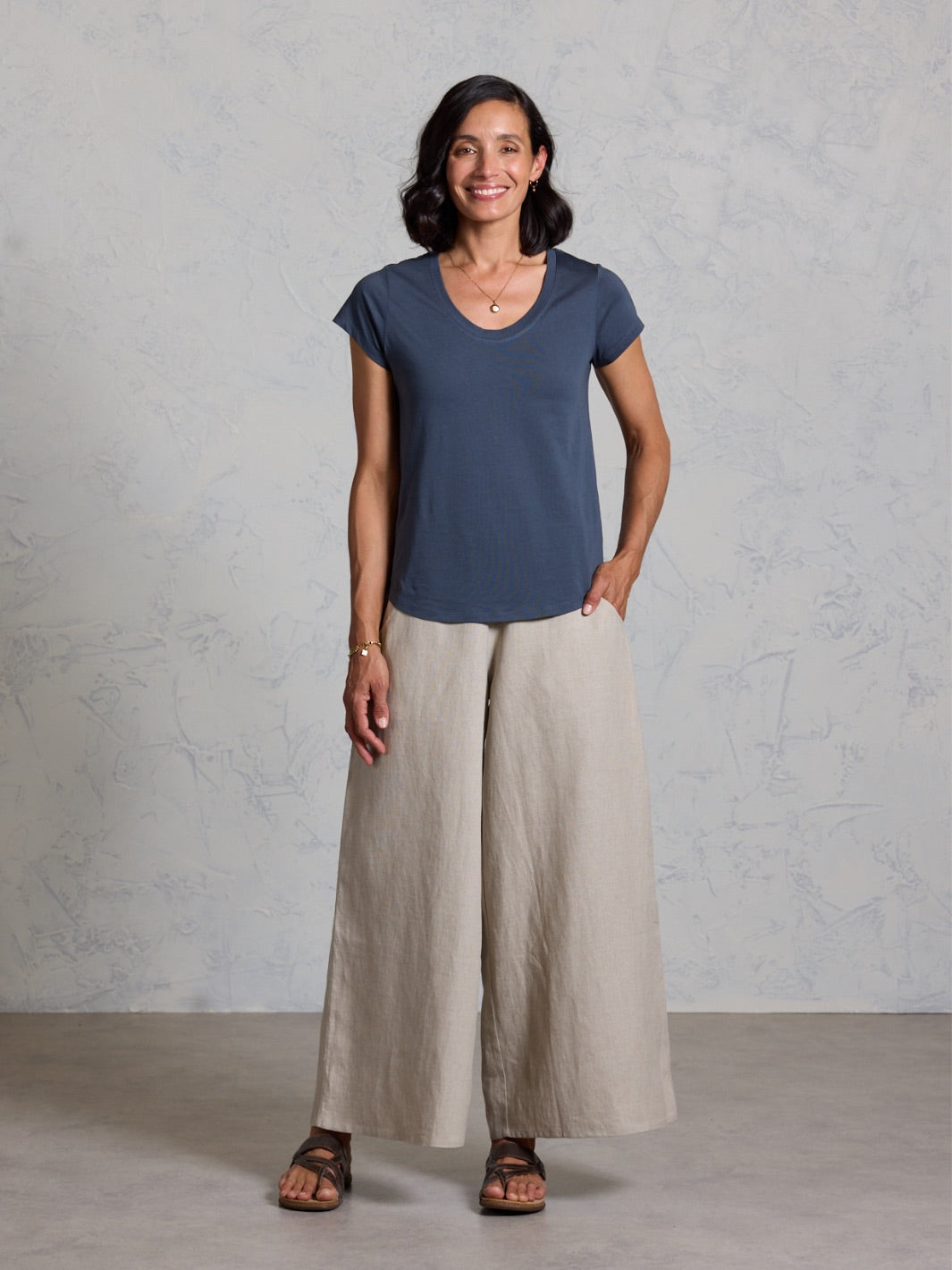 Woman wearing a black top and beige pants against a gray background