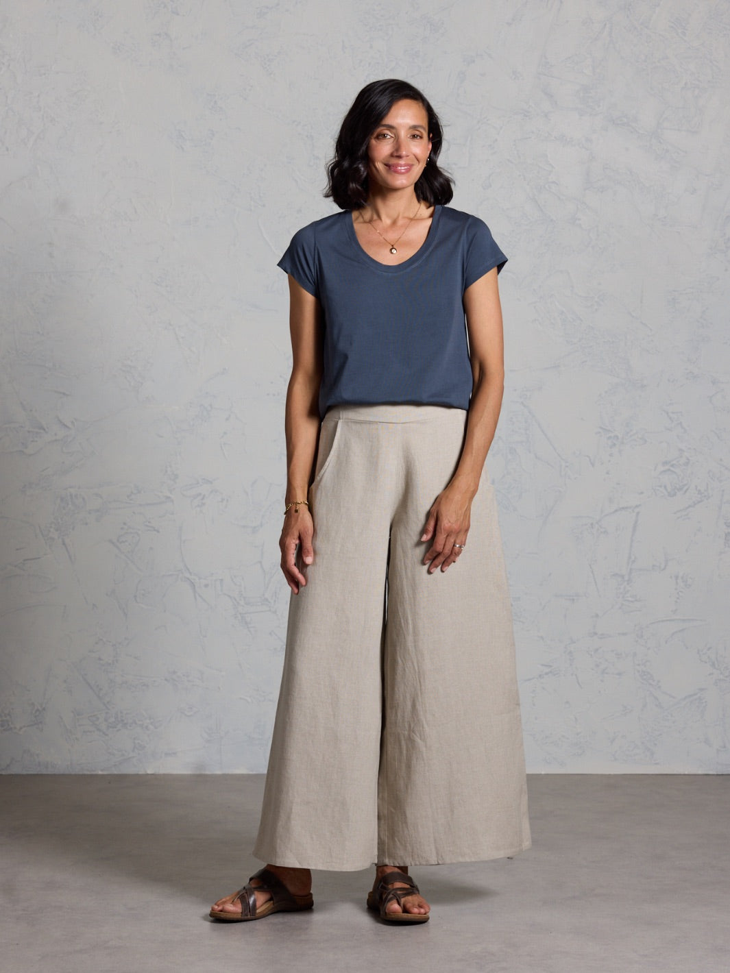 Woman wearing a back top and beige wide-leg pants against a gray background