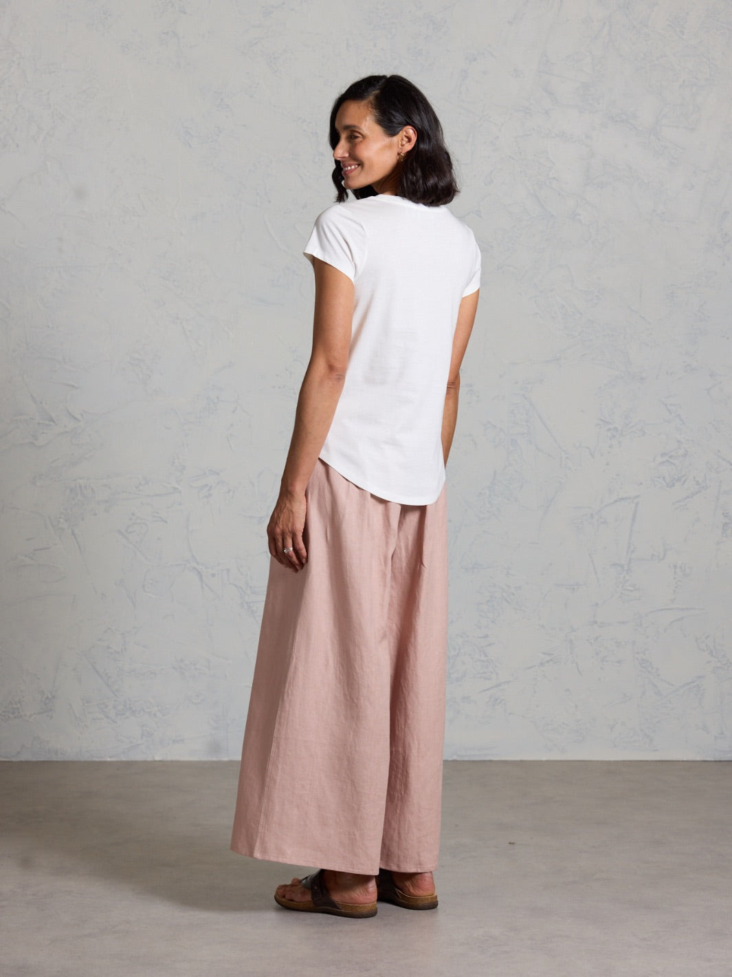 Woman wearing a white t-shirt and pink pants against a plain background