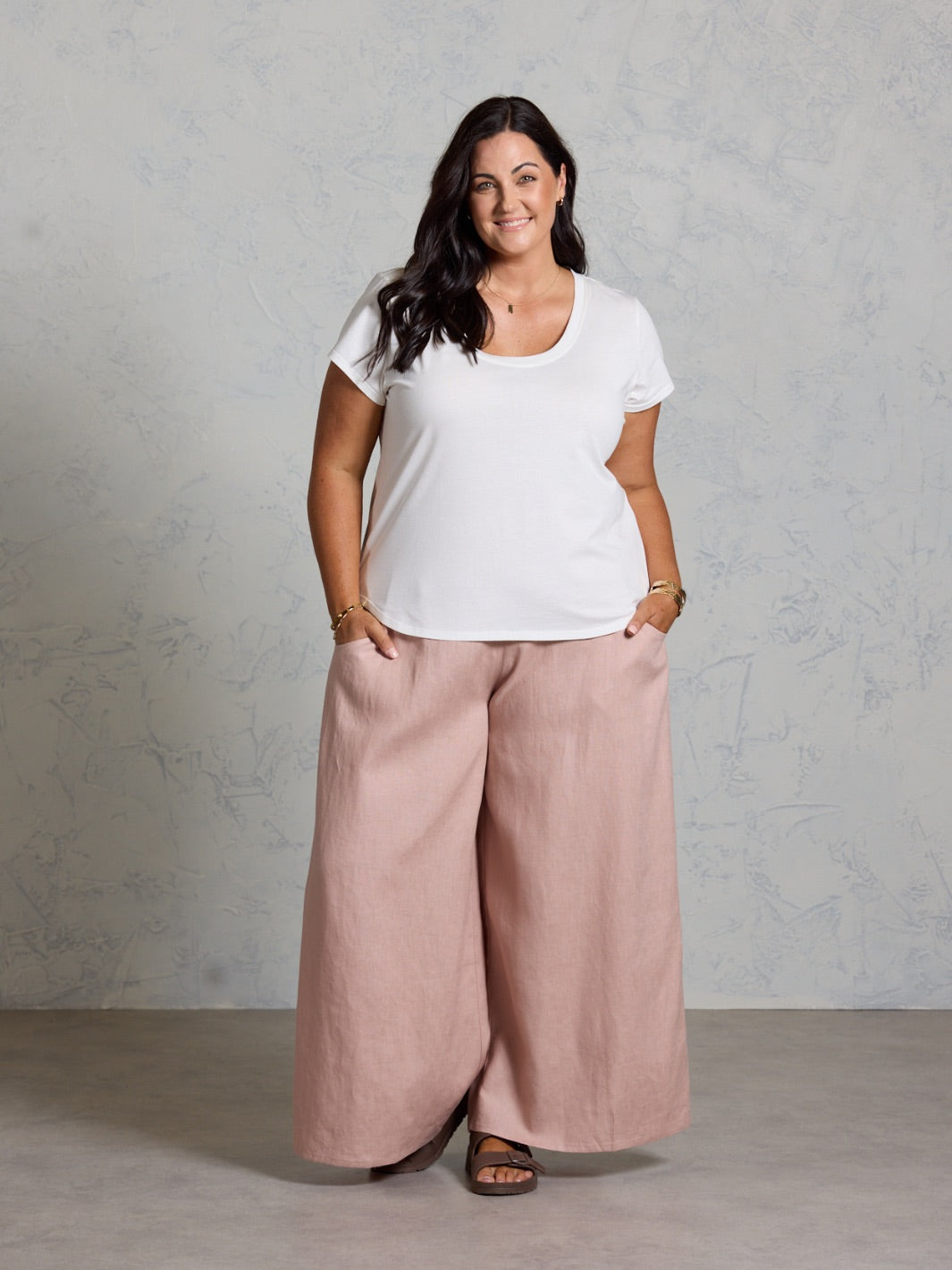 Woman wearing a white t-shirt and pink wide-leg pants against a plain background
