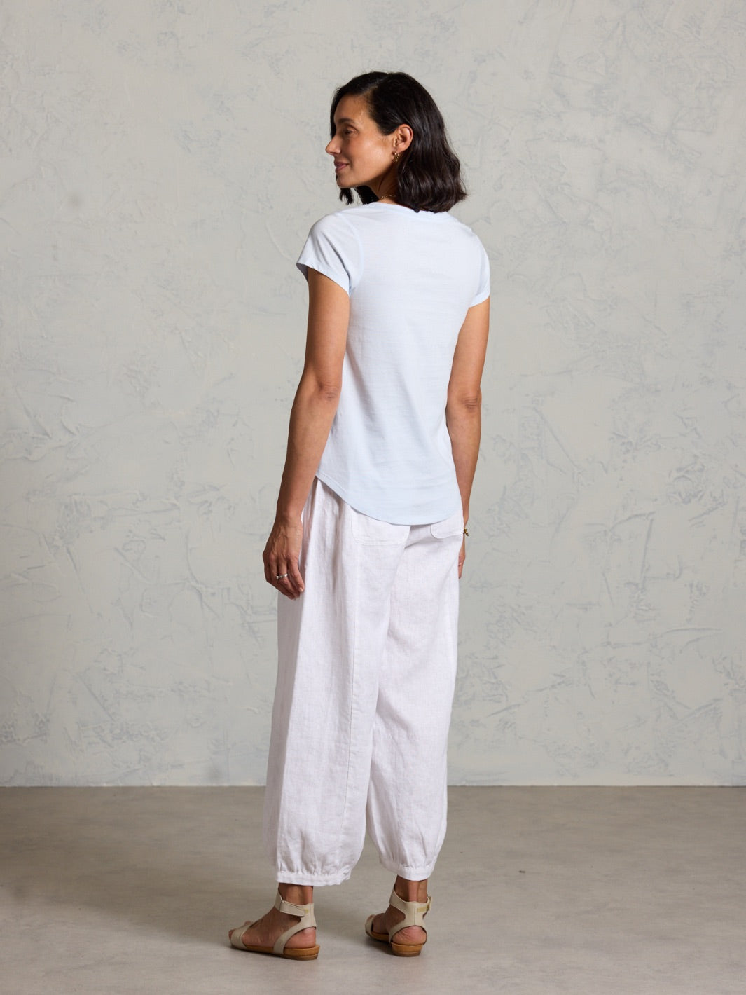 Woman wearing a white t-shirt and light-colored pants against a plain background