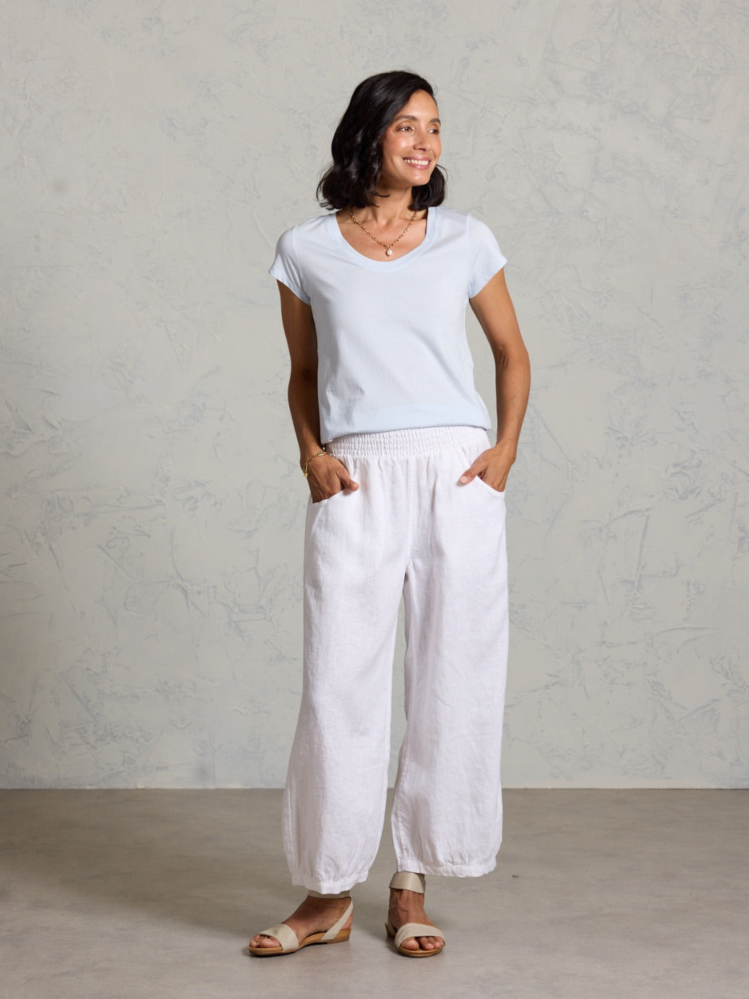 Woman wearing a light blue t-shirt and white pants against a plain background