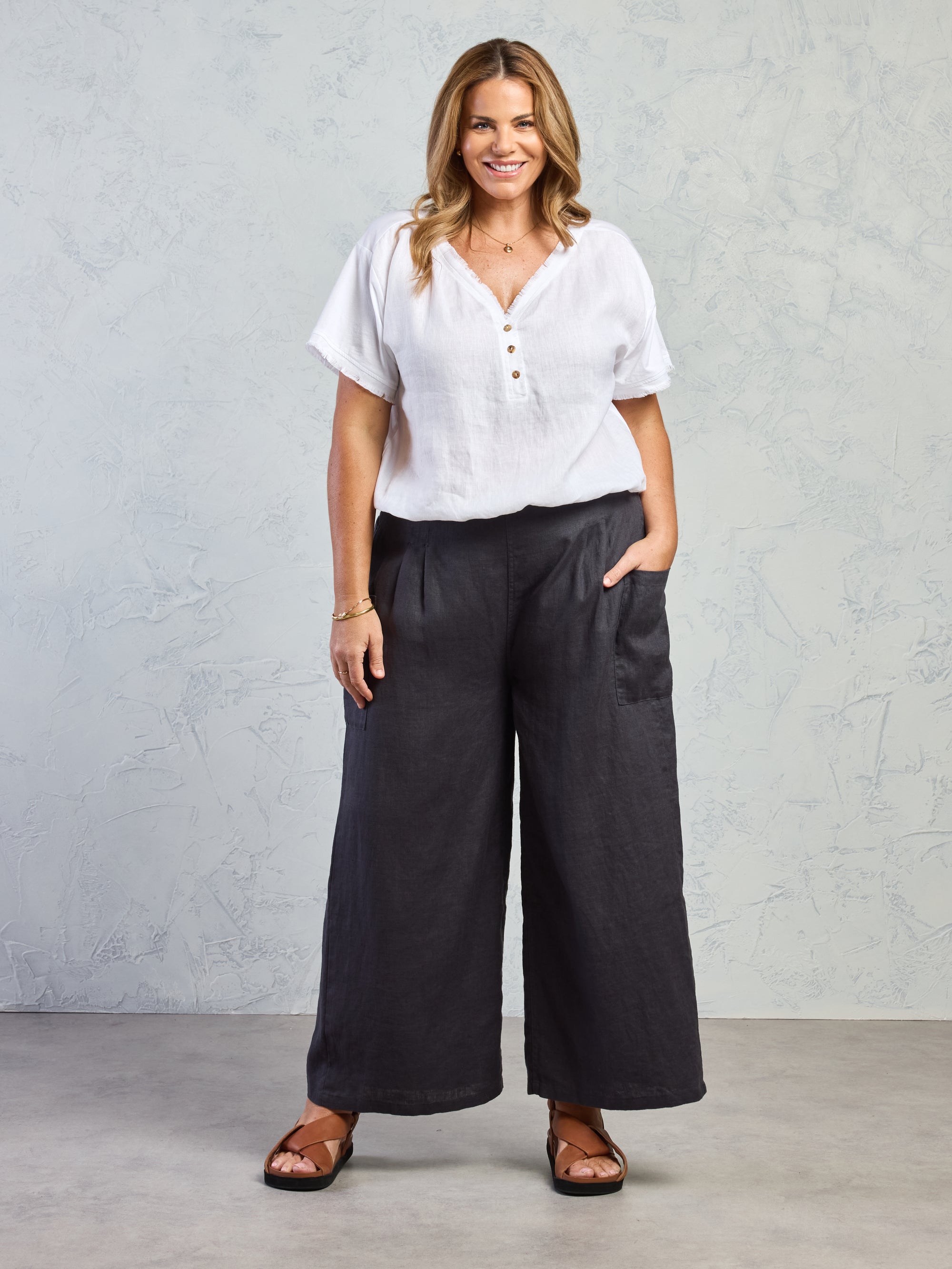 Woman wearing a white blouse and black wide-leg pants against a gray background