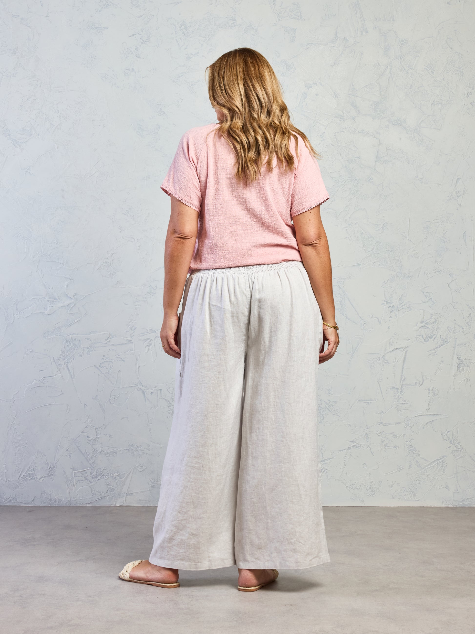 Person wearing a pink top and light gray wide-leg pants against a plain background