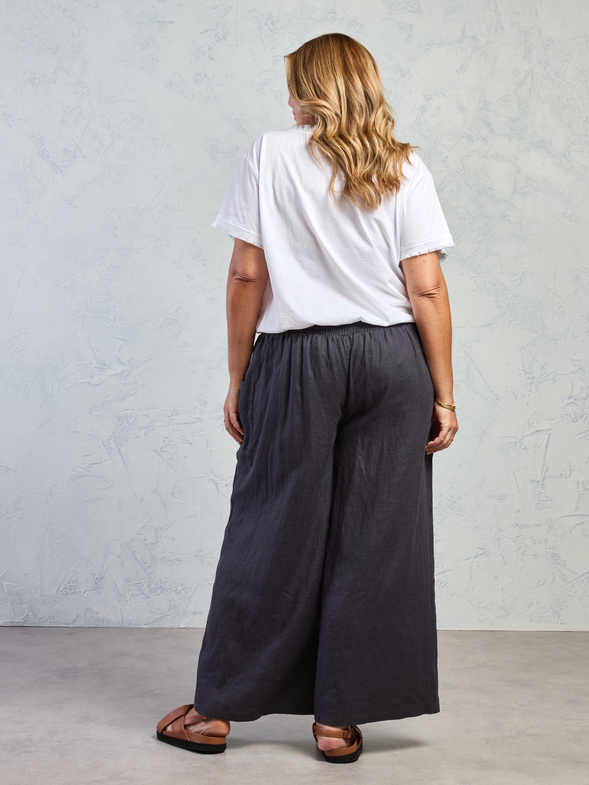 Person wearing a white t-shirt and dark gray wide-leg pants against a plain background