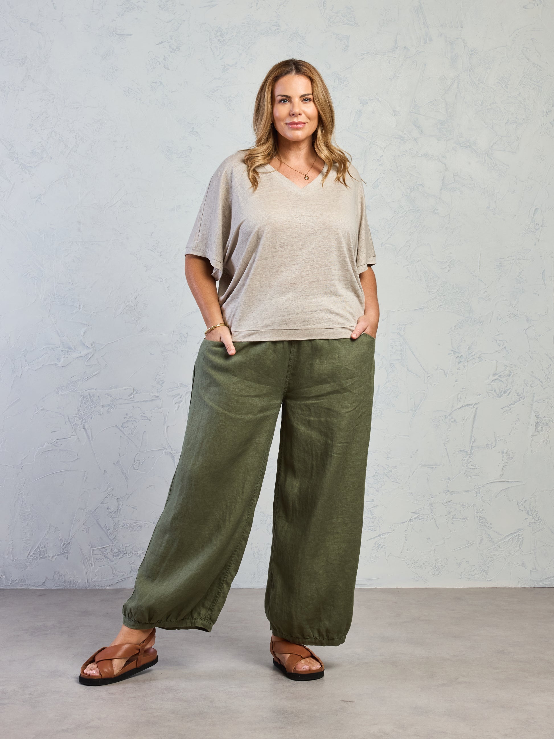 Woman wearing a beige top and green wide-leg pants against a gray background