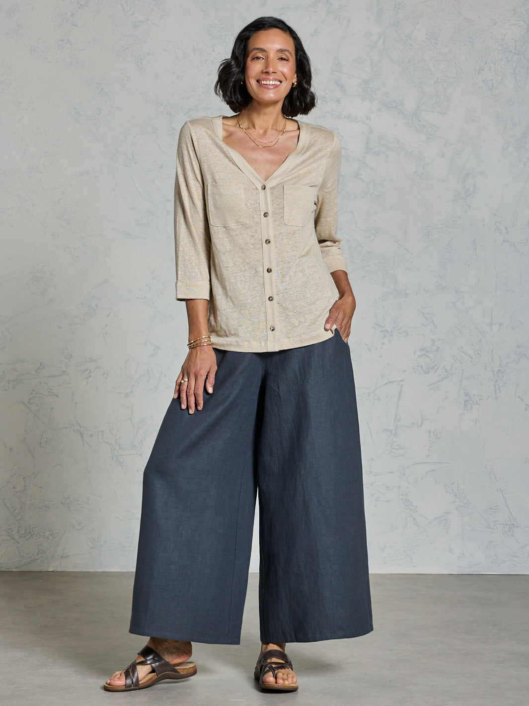 Woman wearing a beige shirt and blue pants against a gray background