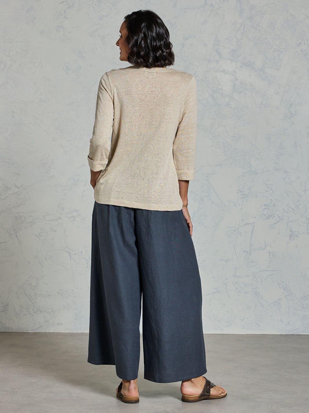 Woman wearing a beige top and blue pants against a gray background