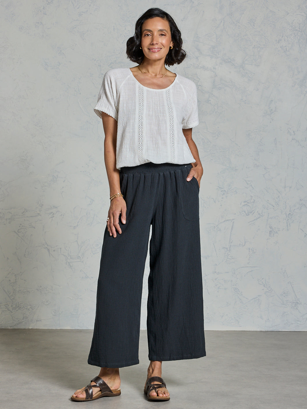 Woman wearing a white top and dark pants against a gray background