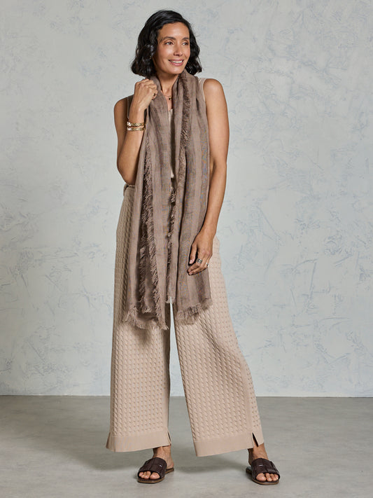 Woman wearing a beige scarf and pants against a plain background