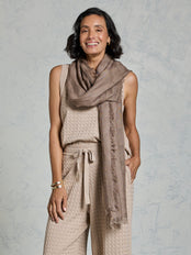 Woman wearing a beige sleeveless top and pants with a matching scarf against a gray background