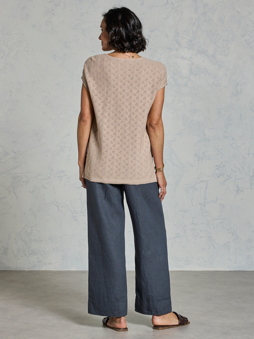 Woman wearing a beige patterned top and dark pants against a light gray background