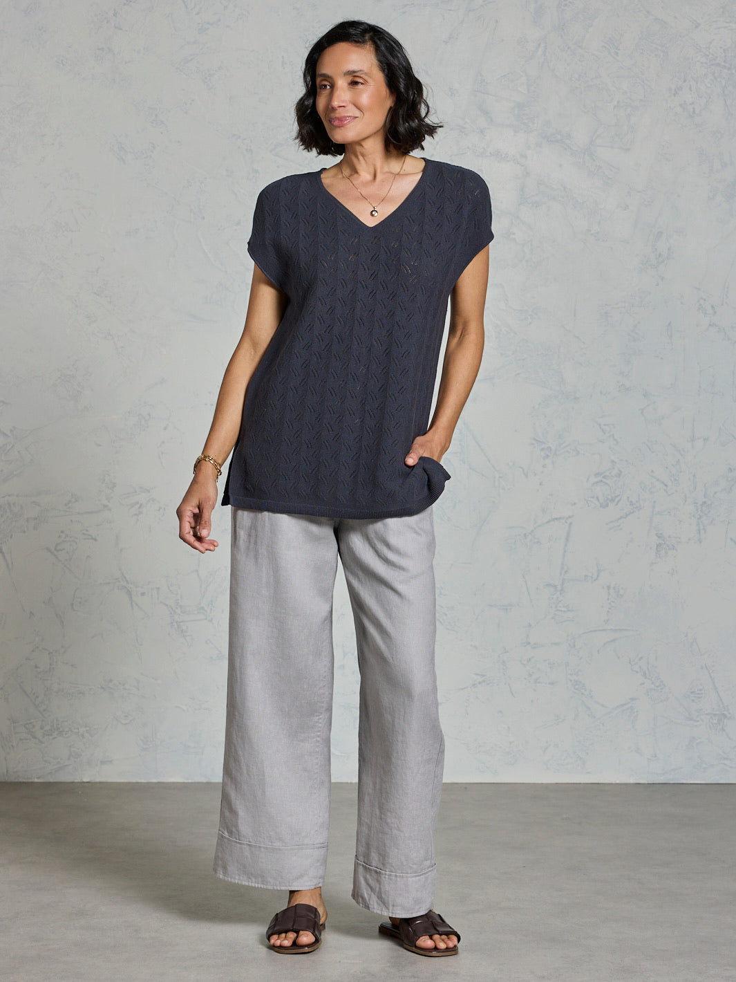 Woman wearing a dark top and light gray pants against a plain background