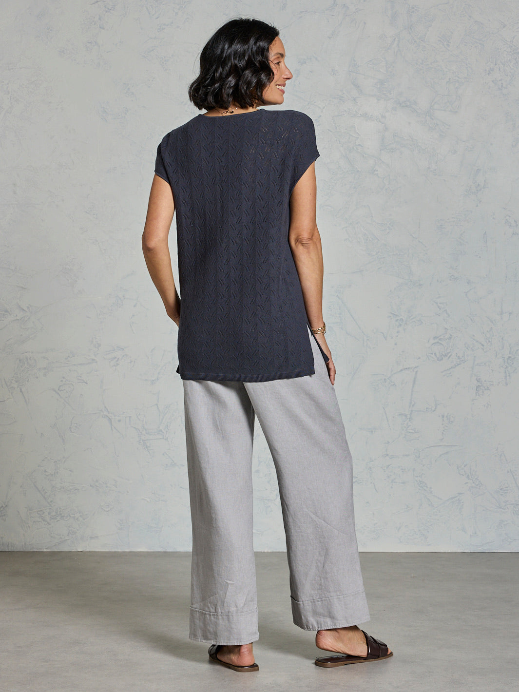 Woman wearing a dark top and light gray pants against a plain background