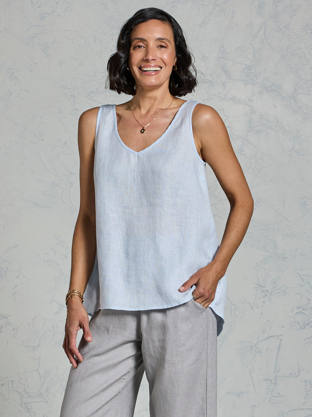 Woman wearing a light blue sleeveless top and gray pants against a plain background