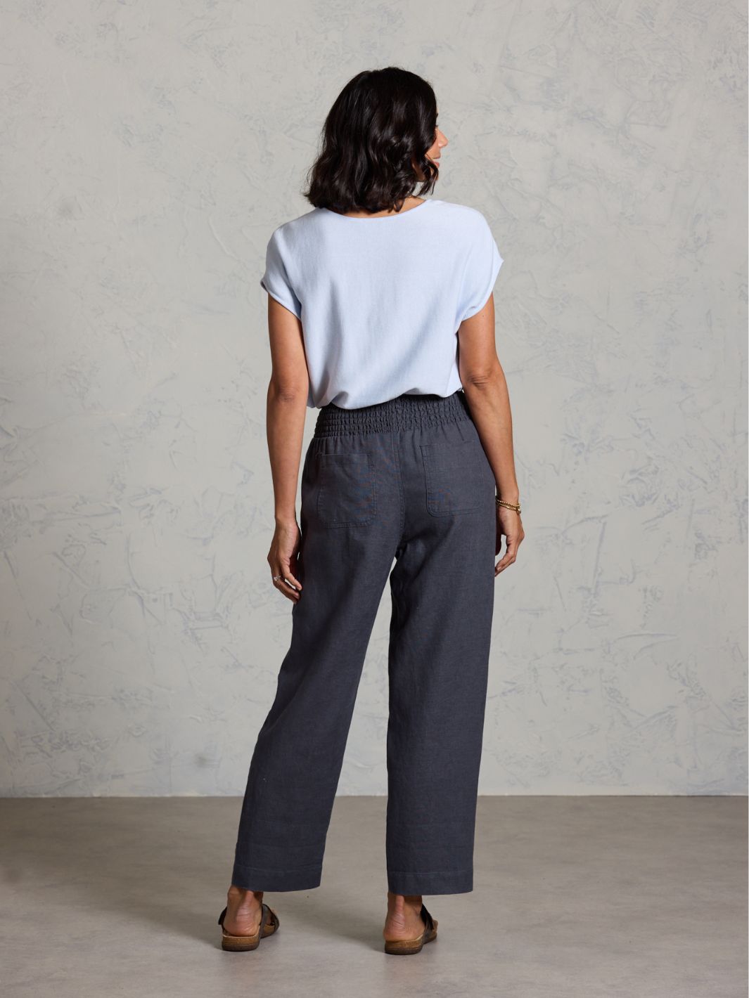 Woman wearing a light blue top and dark gray pants against a plain background