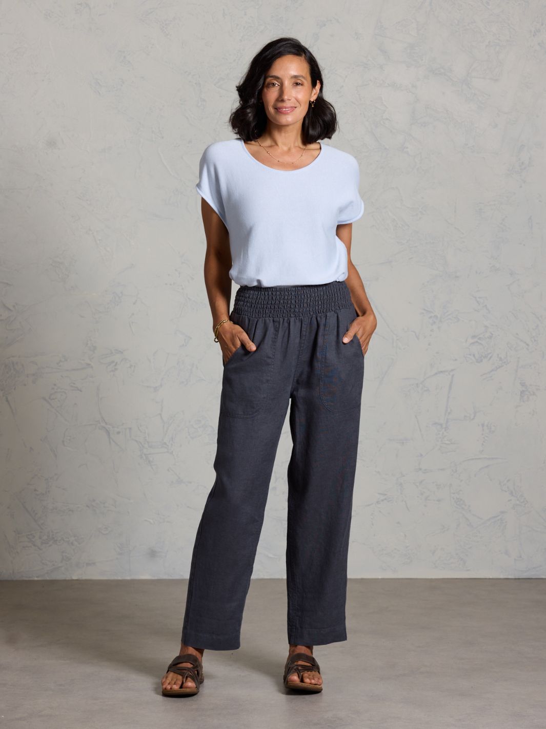 Woman wearing a white top and dark pants against a gray background