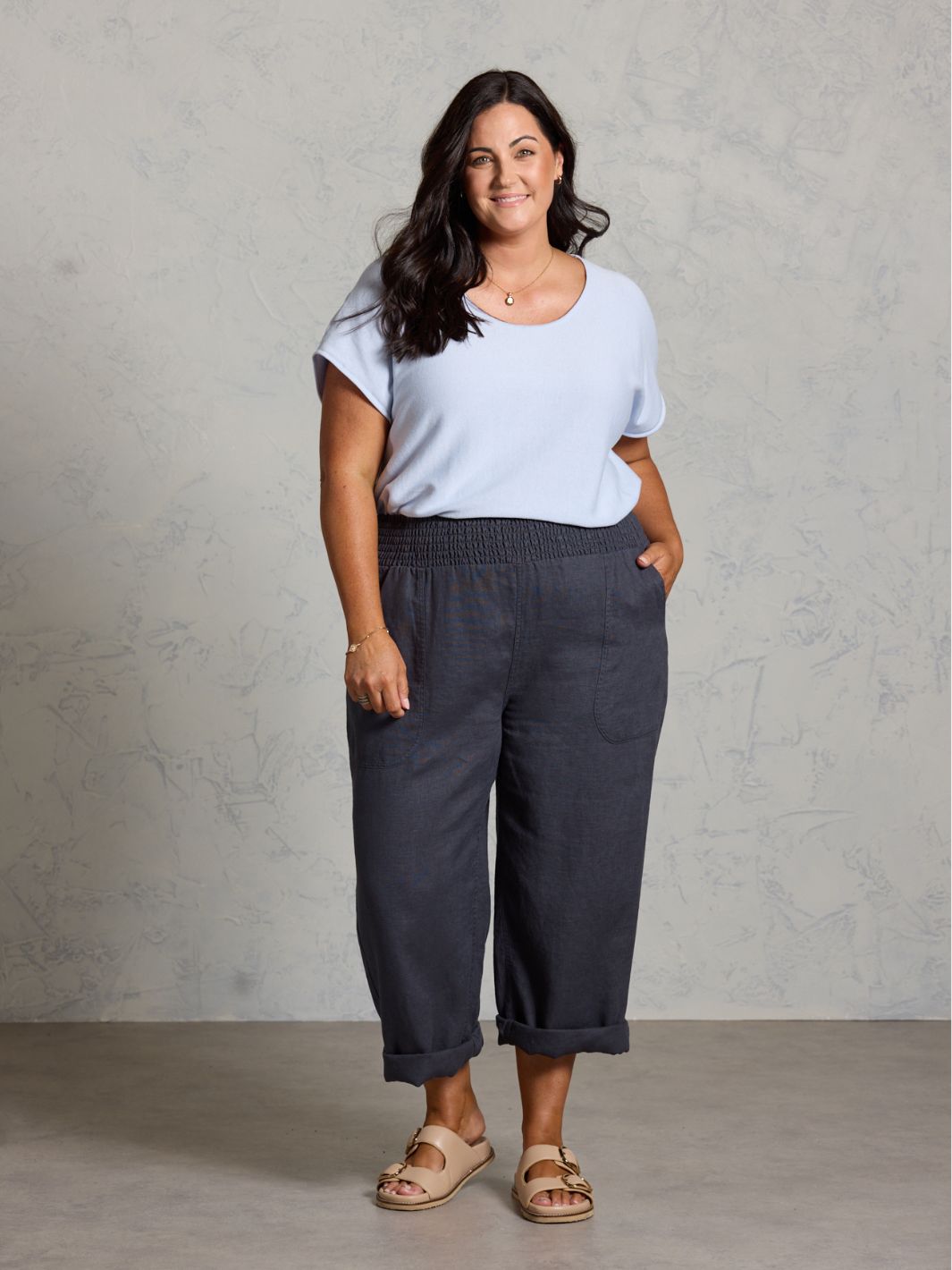 Woman wearing a light blue t-shirt and dark pants against a gray background
