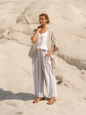 Woman in a white top and striped pants standing on a sandy background