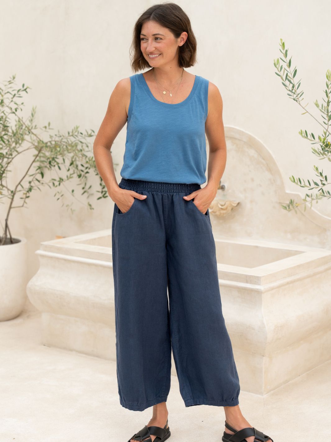 Woman wearing a blue sleeveless top and wide-leg pants standing in a decorative outdoor setting.