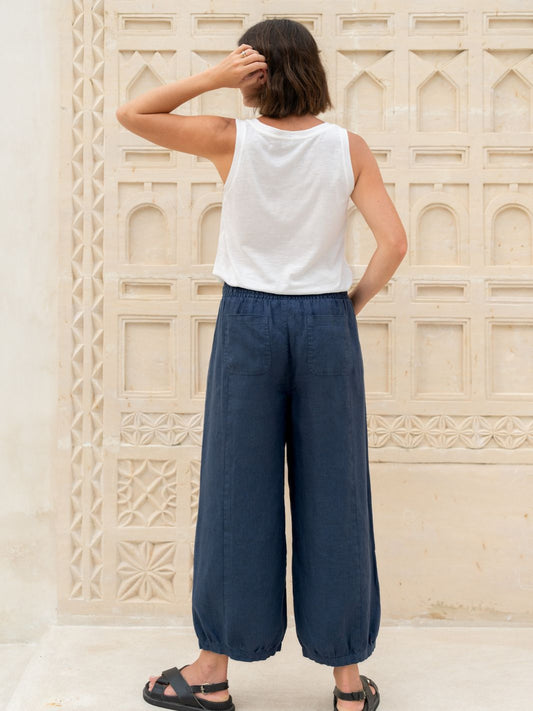 Person wearing a white sleeveless top and blue wide-leg pants standing against an ornate stone wall.