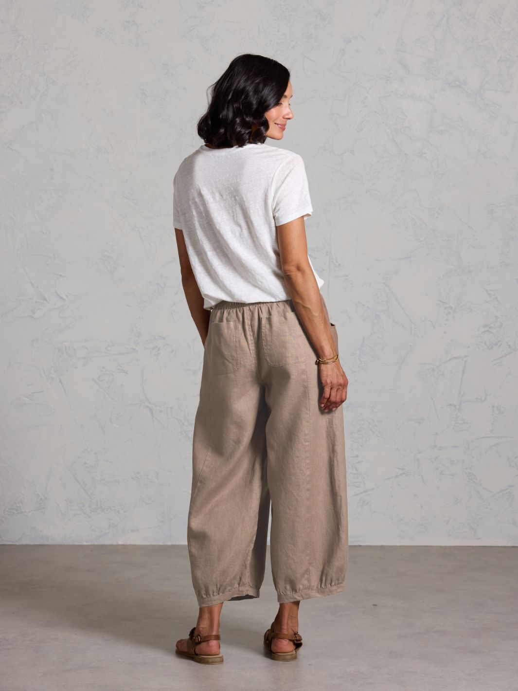 Woman wearing a white t-shirt and brown pants against a plain background