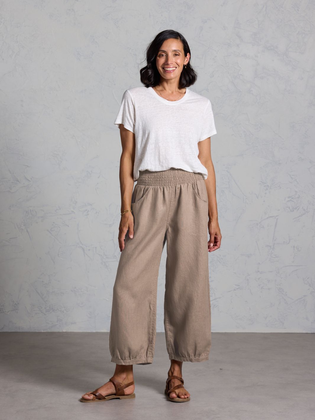 Woman wearing a white t-shirt and brown pants against a gray background