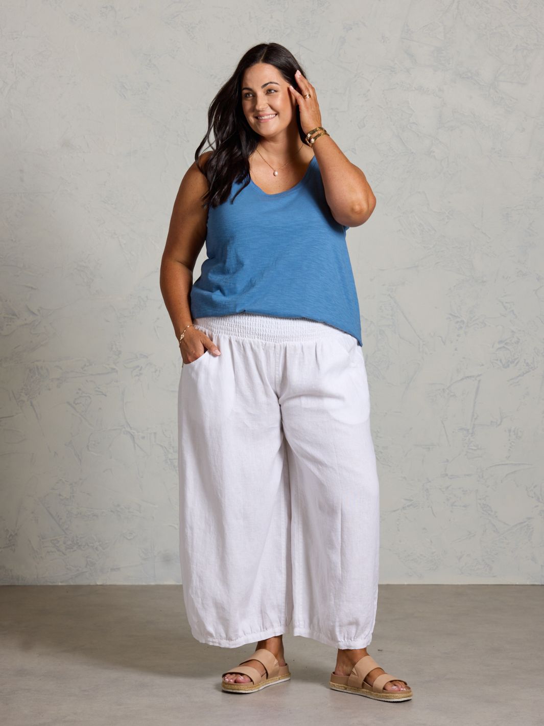 Woman wearing a blue top and white pants against a gray background