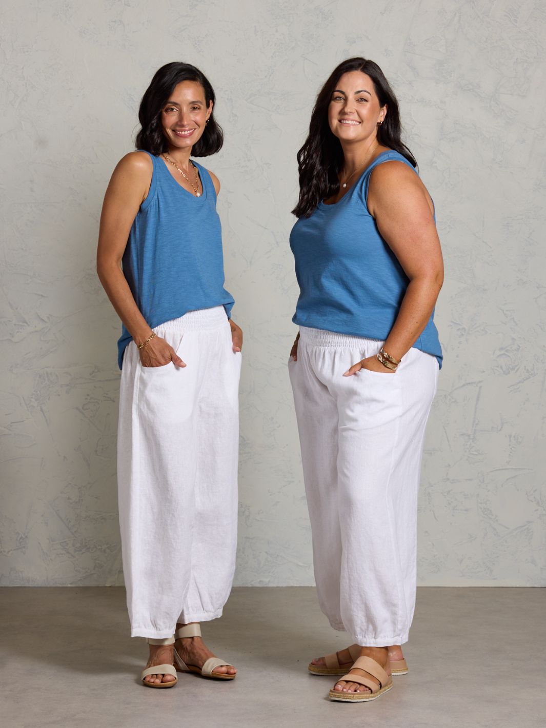 Two women wearing matching blue tops and white pants against a plain background