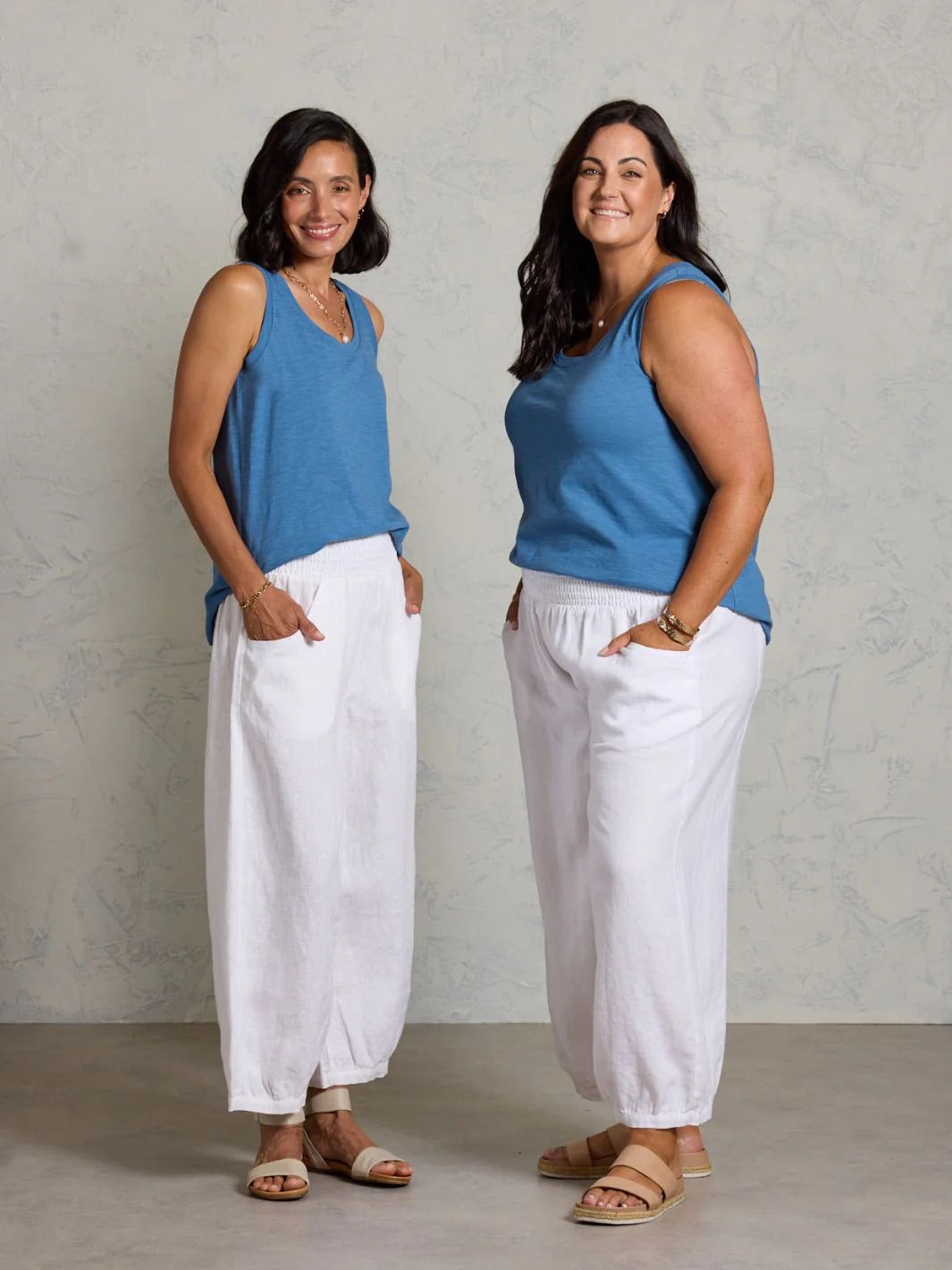 Two women wearing matching blue tops and white pants against a plain background