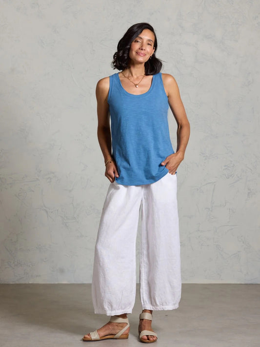 Woman wearing a blue tank top and white pants against a gray background