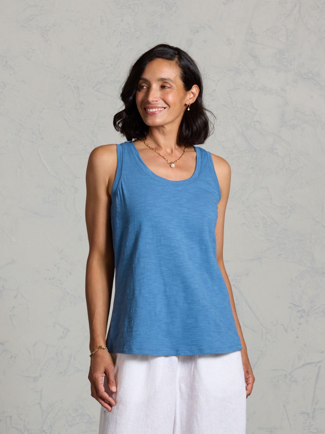 Woman wearing a blue tank top and white pants against a gray background