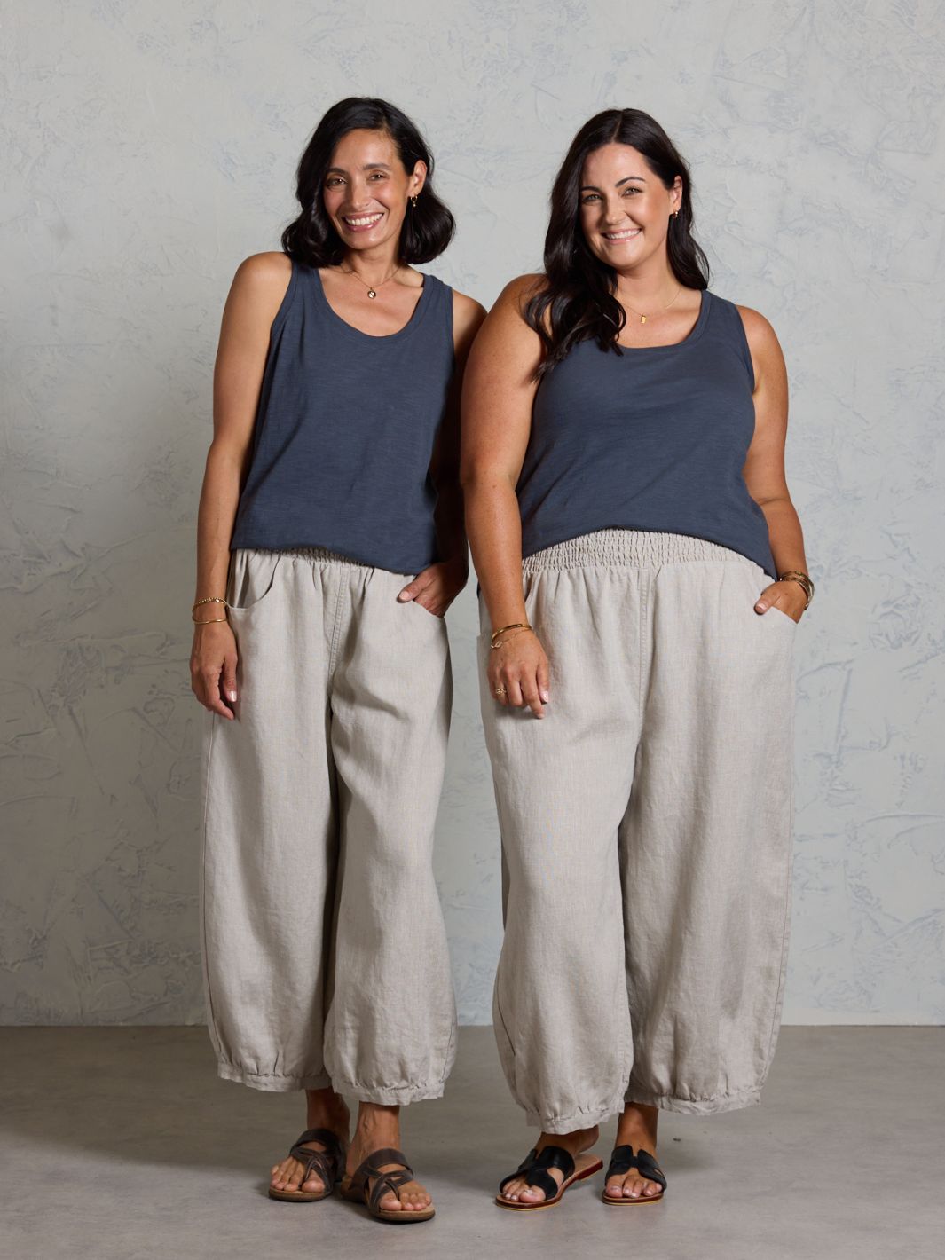 Two women wearing dark tank tops and beige wide-leg pants standing against a plain background.