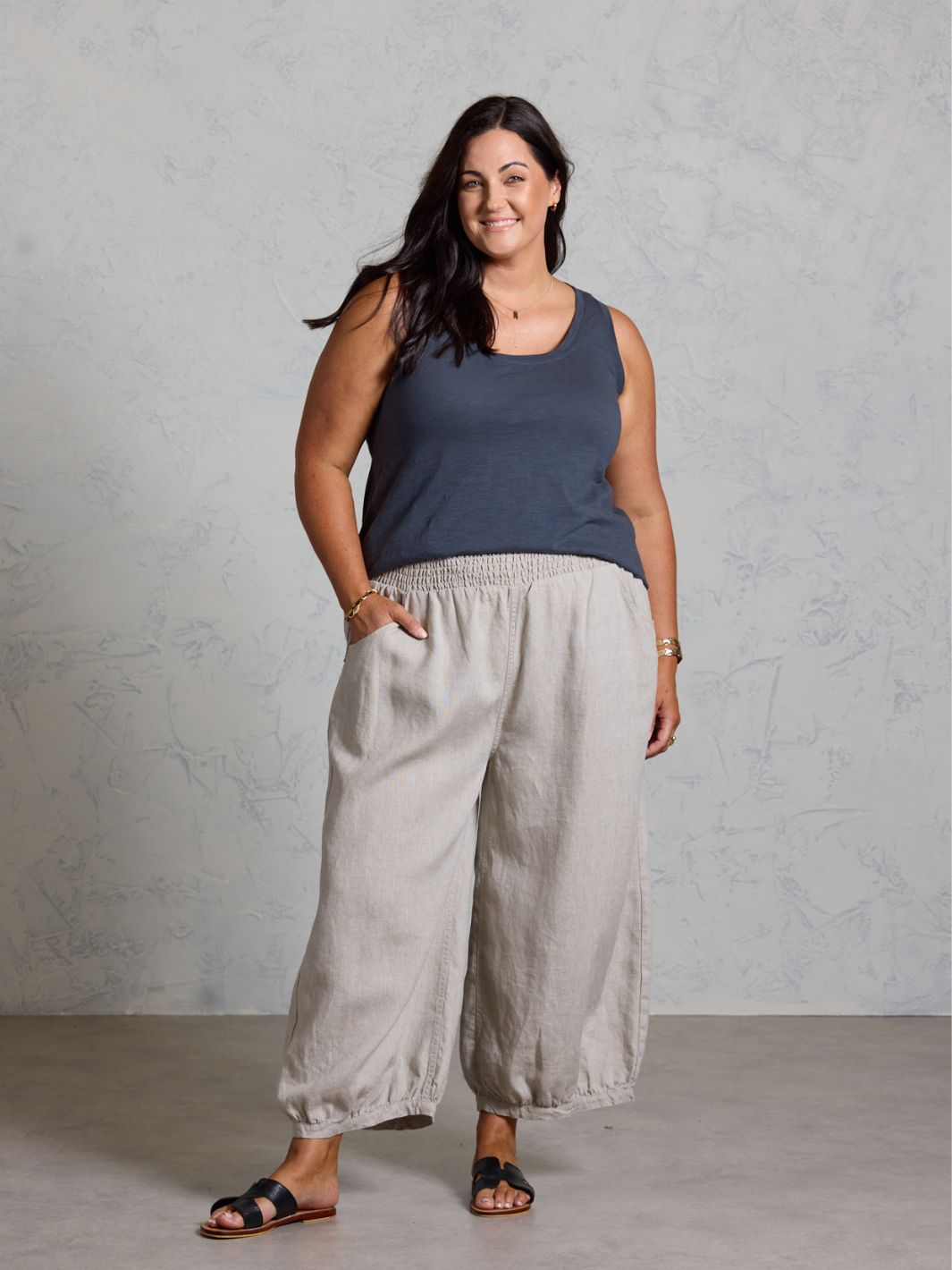 Woman wearing a dark tank top and light gray wide-leg pants against a plain background
