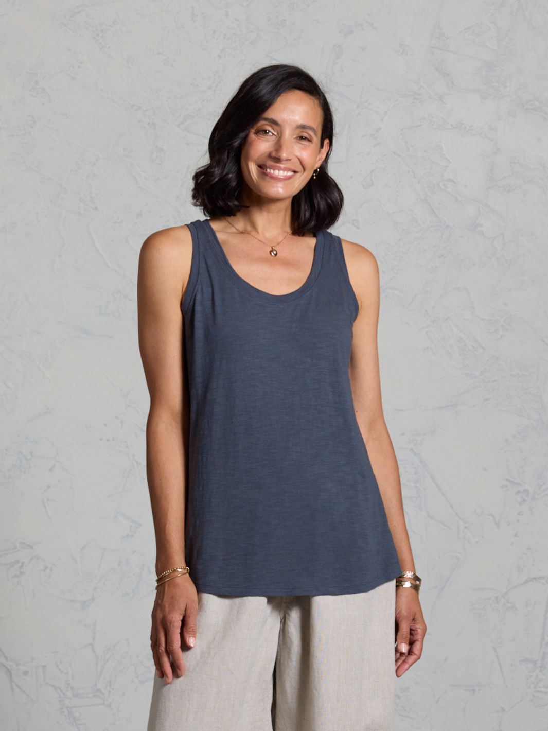 Woman wearing a dark tank top and beige pants against a gray background