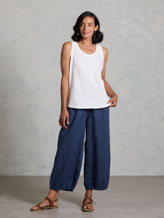 Woman wearing a white sleeveless top and dark pants against a gray background