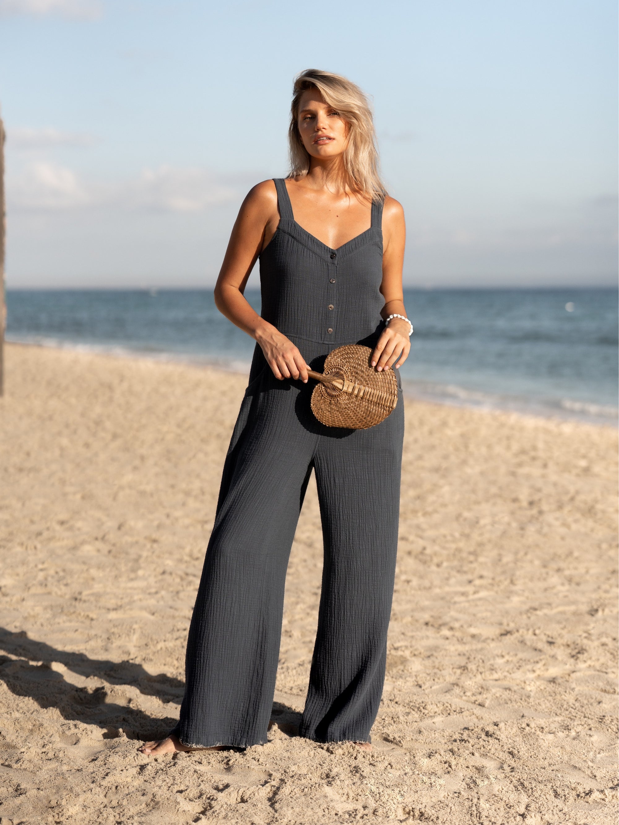A woman wearing a charcoal cotton jumpsuit and standing on a beach